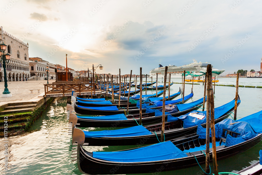 Pier gondolas near Piazza San Marco in Venice at sunrise against the background of a cruise ship swims. A number of boats on the background of the waterfront in Venice. Italy.