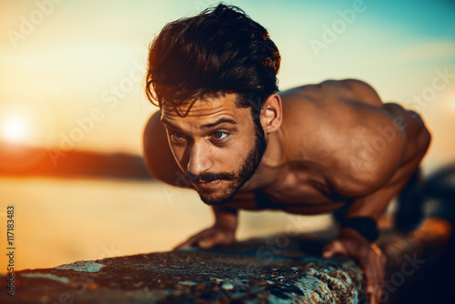 Fotografie Young athletic man doing push ups outdoors