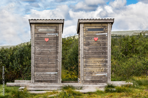 Tableau sur toile Two wooden outhouse toilets with red heart in mountain landscape