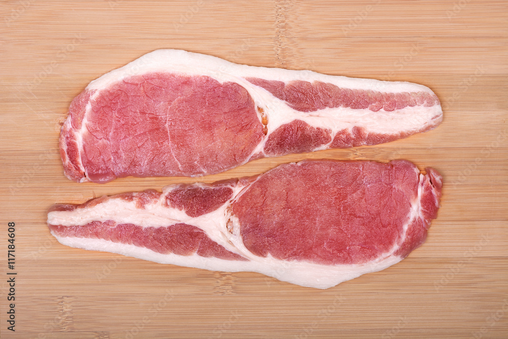 Raw bacon slices on a wooden cutting board. From above. Raw bacon slices on a wooden cutting board. From above.