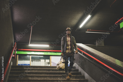 Young handsome afro black man going downstairs in the underground, holding a bag, overlooking left - youth, transport concept