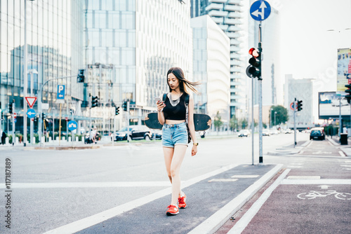 Young beautiful asian woman skater with backpack walking outdoor in the city using smart phone hand hold - technology, social network, communication concept