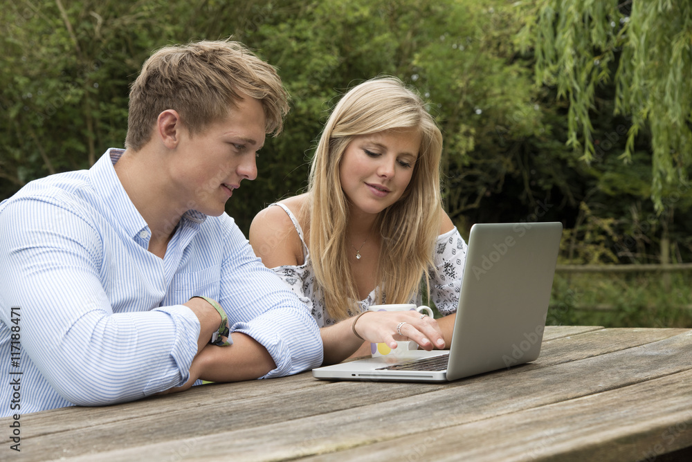 TEENAGERS USING A COMPUTER - JULY 2016 -  A teenage couple using a computer on a garden table