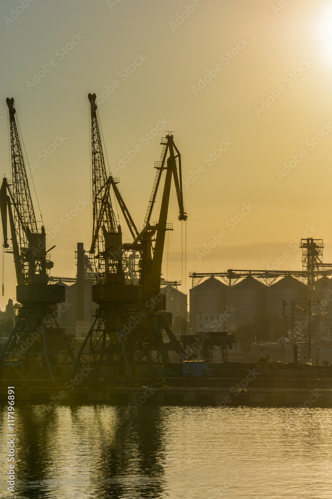 Port cranes against the evening sky in yellow tones on sunset