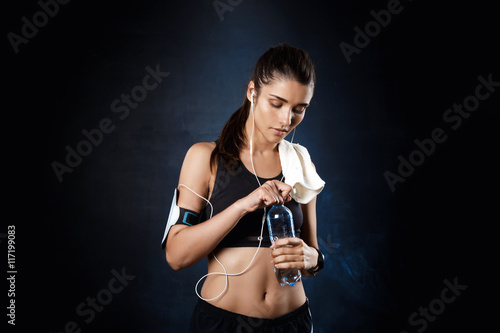 Young beautiful sportive girl holding water over dark background. photo