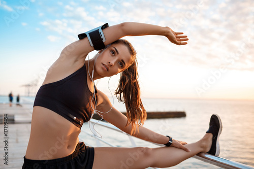 Young beautiful sportive girl training at sunrise over seaside. photo