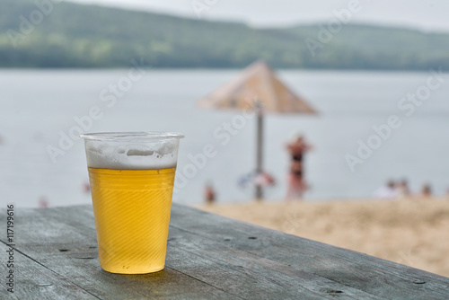 пластиковый стакан пива на деревянном столе на пляже