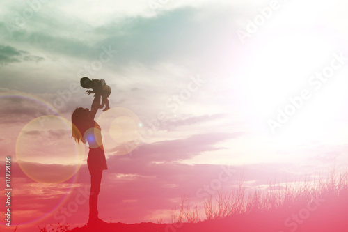 Mother holding baby walking on the sunset background.