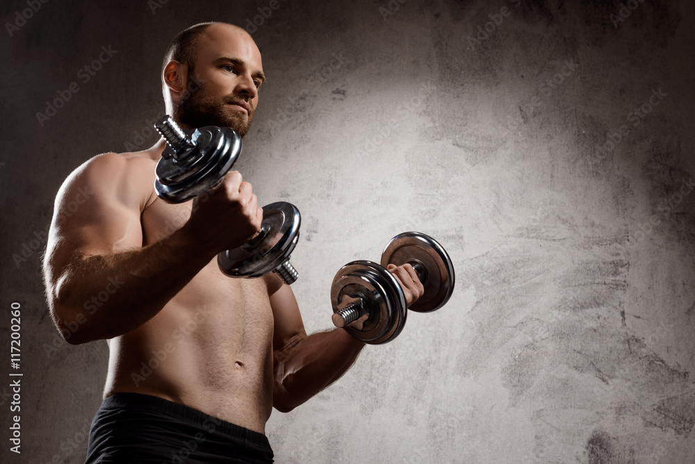 Young powerful sportsman training with dumbbells over dark background. Young powerful sportsman training with dumbbells over dark background.