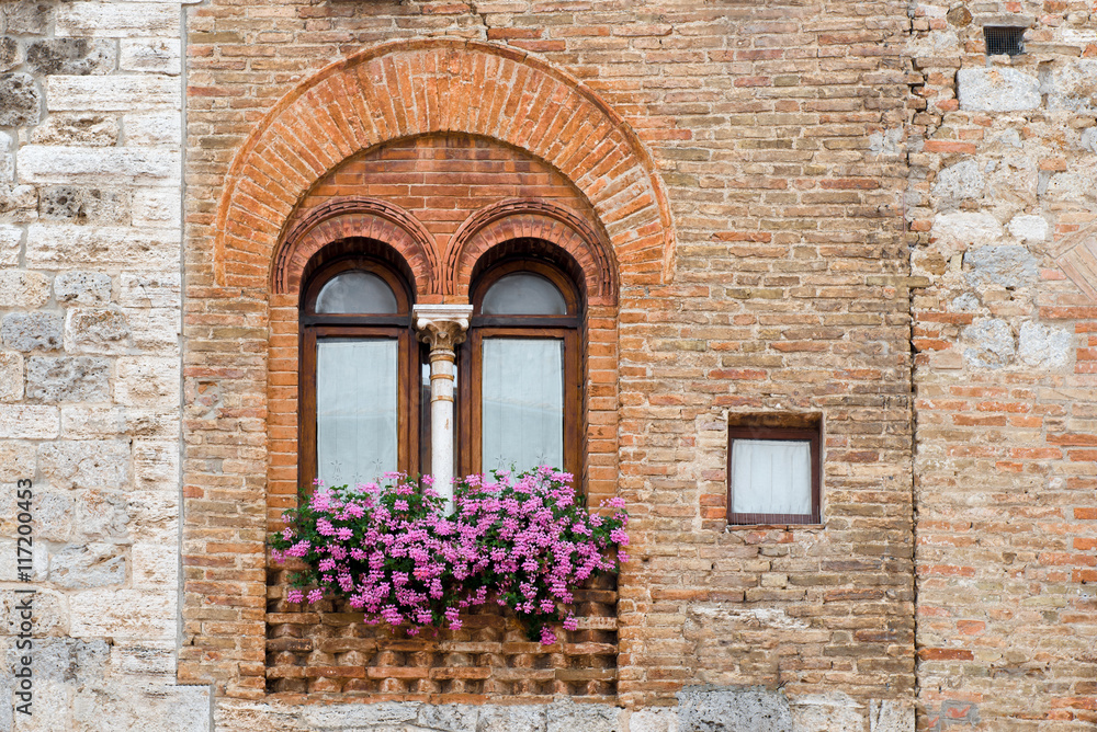 Ancient window with flowers in the medieval town San Gimignano in Tuscany, Italy.