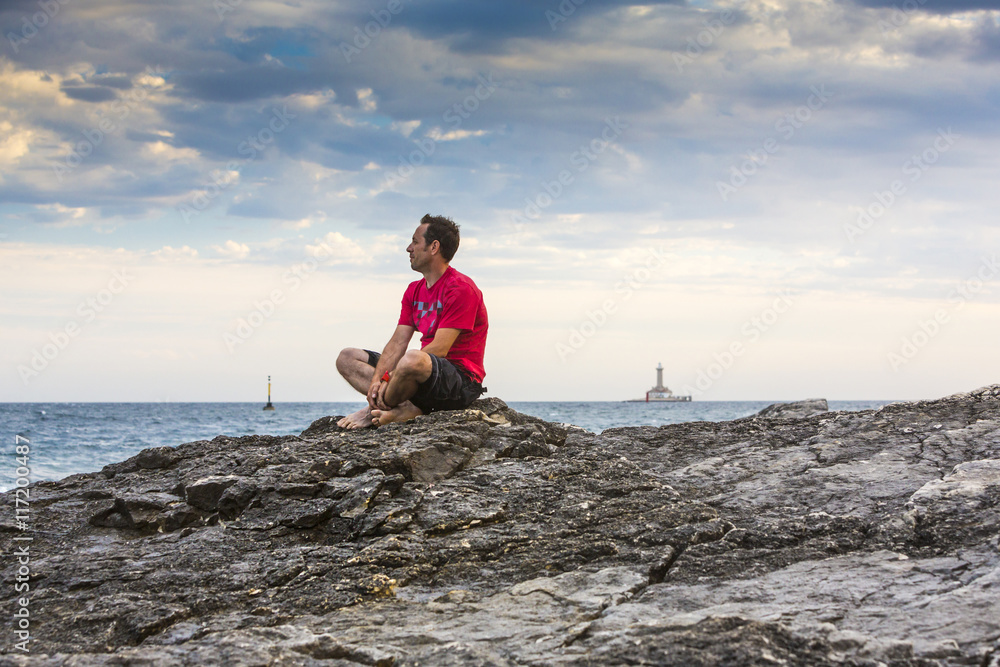 Kroatien, Istrien, Kap Kamenjak, Mann sitzt auf den Felsklippen und schaut entspannt auf die Brandung