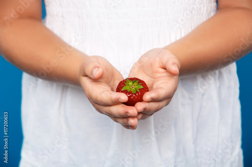 Close up of girl's hand holding strawberry over blue background.