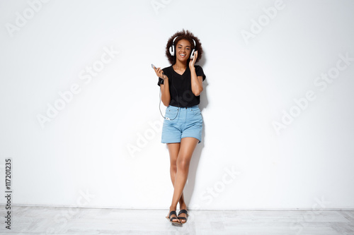 Beautiful african girl listening music in headphones over white background.