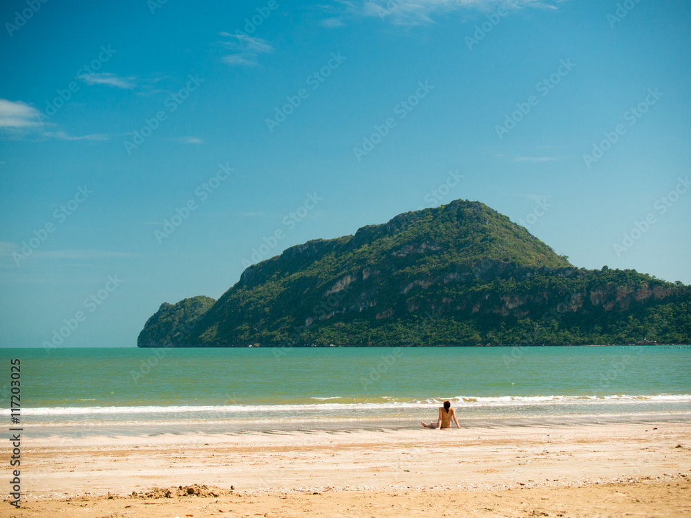 Toned image of a woman sits on the beach during low tide on the background of the islands with trees and sky with clouds Toned image of a woman sits on the beach during low tide on the background of the islands with trees and sky with clouds