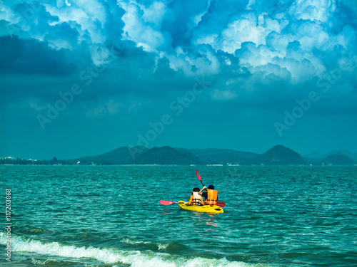 Toned image of a yellow kayak with two tourists sails on the sea on the background of dramatic sky with cumulus clouds