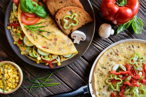 Omelet with pepper, tomato, corn, green onion, cucumber, mushrooms and fried bread on a wooden background