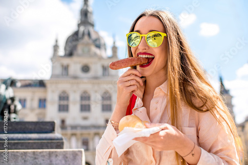 Young female traveler eating sausage on the central square in Graz. Austrian traditional street food