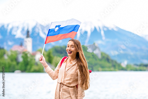Young female tourist with slovenian flag standing near Bled lake, popular tourist destination in Slovenia. Promoting tourism in Slovenia