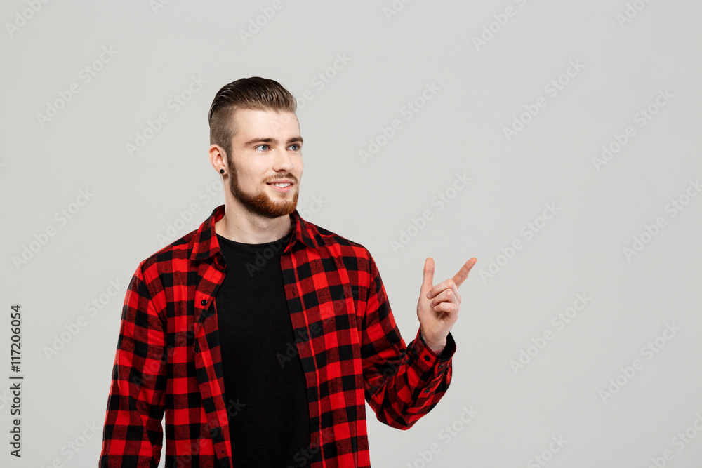 Young handsome man pointing finger in side over grey background. Young handsome man pointing finger in side over grey background.