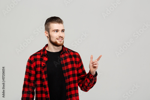 Young handsome man pointing finger in side over grey background.