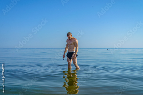 A man in a loincloth standing in water with a knife in his hand.