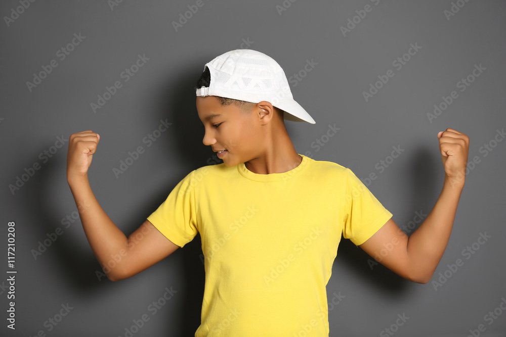 African American boy showing biceps on grey background