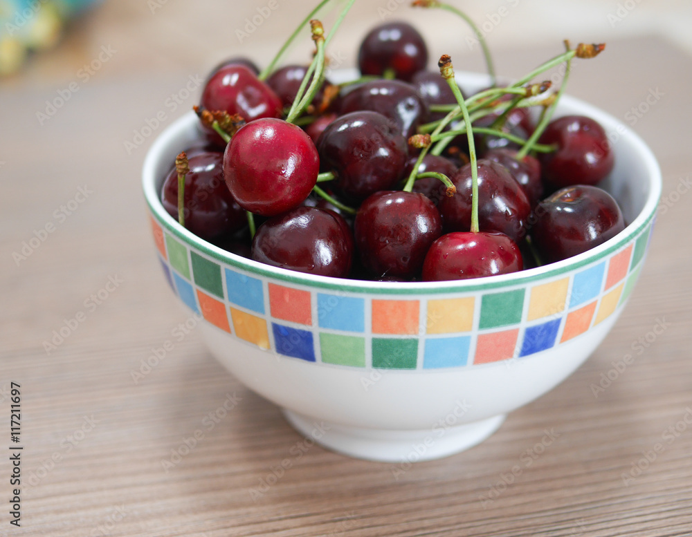 Cherries in colorful bowl on wooden surface Cherries in colorful bowl on wooden surface