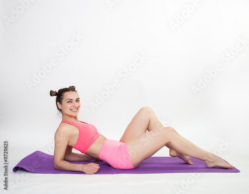 Young brunette woman doing pilates exercises on mat studio background