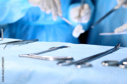 Surgical tools lying on the table while group of surgeons at background operating patient. Steel medical instruments ready to be used.