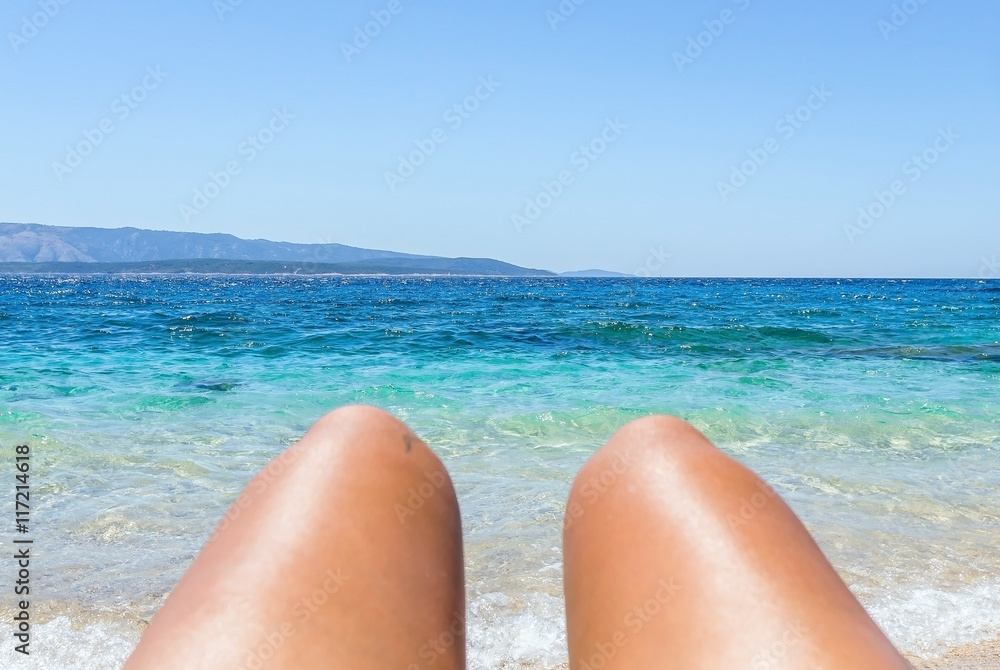 View of clear sea water on island in Croatia through female legs in summertime on vacation View of clear sea water on island in Croatia through female legs in summertime on vacation