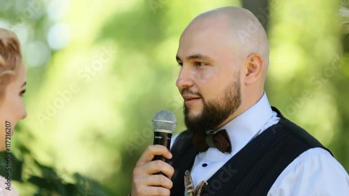 Handsome elegant bald groom taking vows at the outdoors wedding ceremony