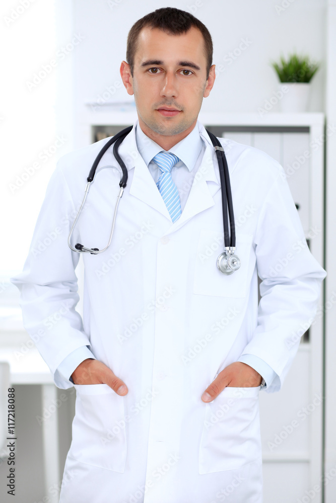 Friendly male doctor in the hospital office. Ready to examine and help patients. High level and quality medical service concept. Friendly male doctor in the hospital office. Ready to examine and help patients. High level and quality medical service concept.
