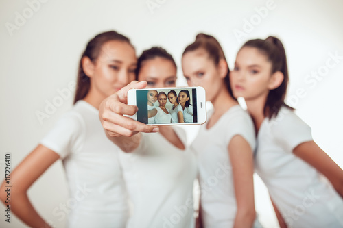 Positive friends portrait of four happy girls making selfie  sure funny faces  grimaces  joy  emotions  casual style  pastel colors  white wall. crazy funny woman. White background.
