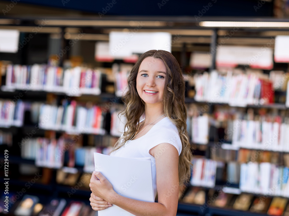 Happy female student holding books at the library Happy female student holding books at the library