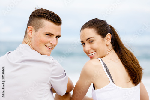 Young couple looking at camera while sitting next to each other on beach