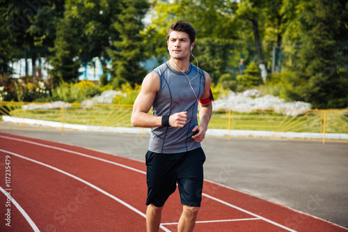Young sports man running down stadium track with earphones