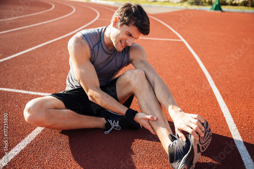 Young male runner suffering from leg cramp on the track photo