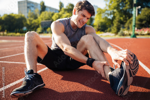 Fotografie Young male runner suffering from leg cramp on the track
