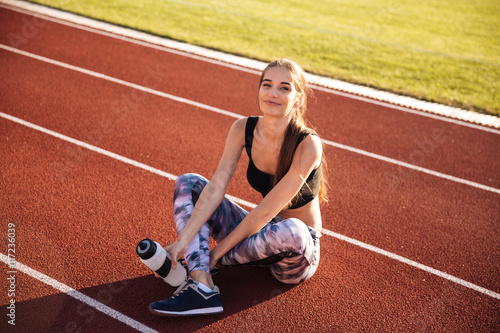 Fitness woman sitting on running track and holding water bottle