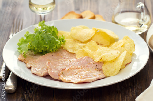 fried meat with potato chips and fresh salad on white dish on brown wooden background