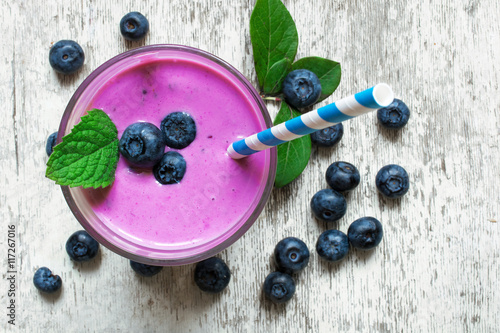 Blueberry smoothie in a glass with a straw and mint and fresh berries