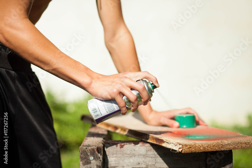 Hand of young man spraying small piece of wood by green colour;