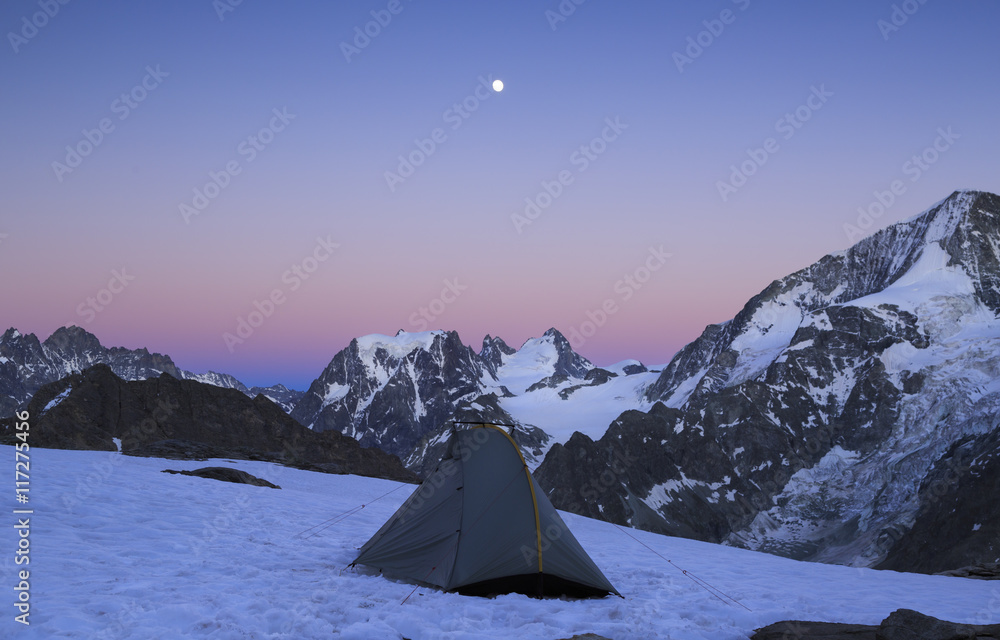 The moon rising above a tent in the mountains in Wallis, Switserland. Outdoor and adventure concept.