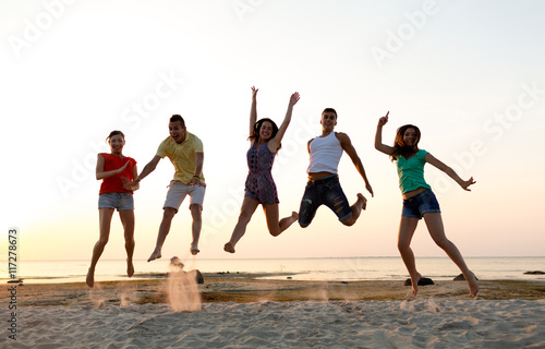 smiling friends dancing and jumping on beach