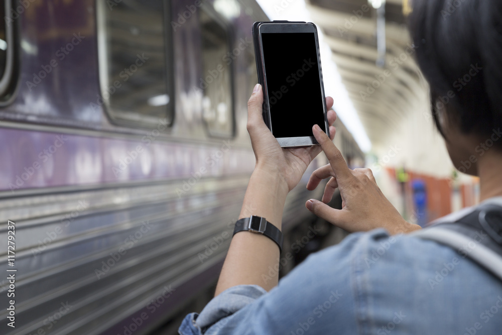 woman holding smartphone with backpack at train station