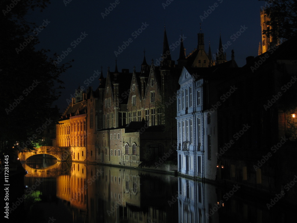 Nighttime shot of one of the canals in Bruges (Brugge) Belgium with canalside houses illuminated in different colours, which in turn are reflected in the still waters of the canal