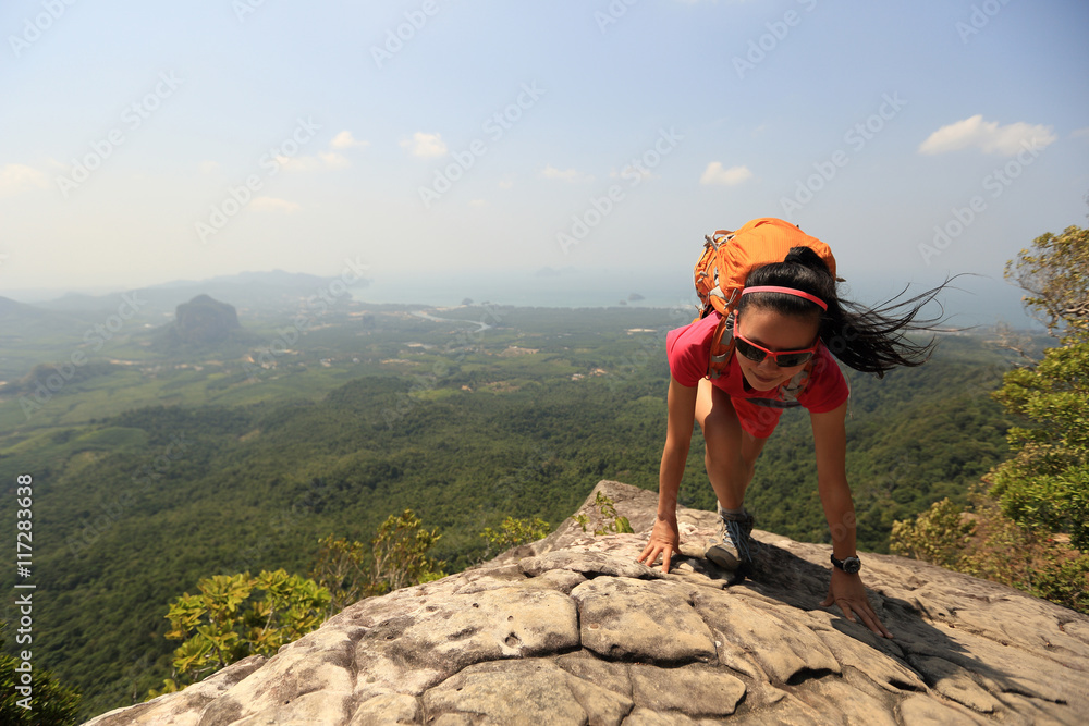 young asian woman hiker climbing rock on mountain peak cliff