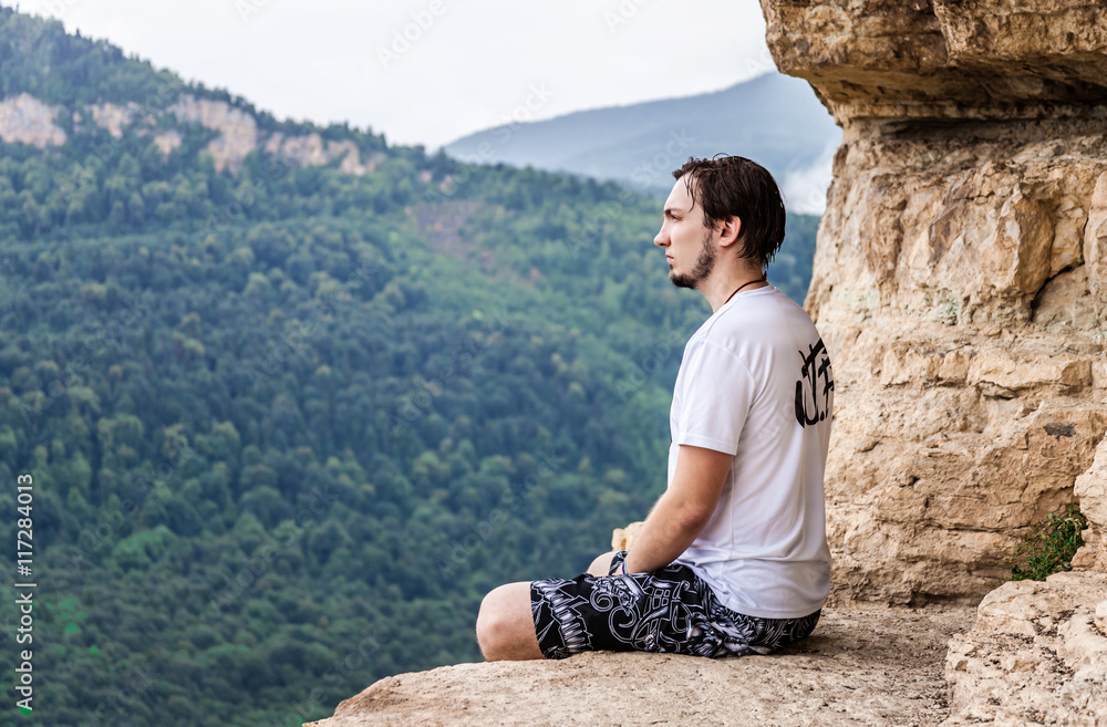 Naklejka premium Man sitting on top of a mountain and enjoying a valley view