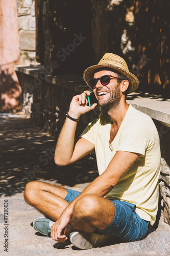 Young hipster man talking on the smartphone sitting on the ground
