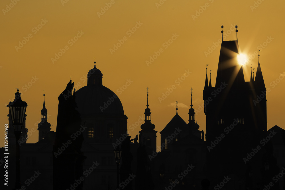 Golden silhouette of the Prague Charles Bridge and towers and churches with sun ray over the bridge tower.